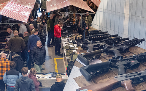 Foto's van replica's op een tafel tijdens een airsoftbeurs en de tweedehandsmarkt.